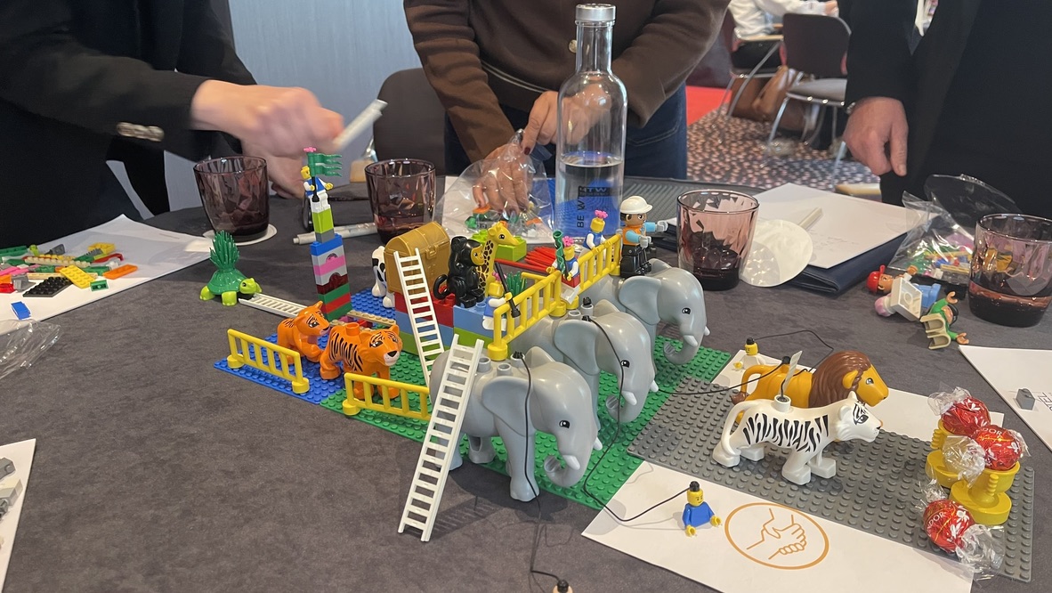 Participants' hands around an interconnected LEGO model built during a facilitated session.